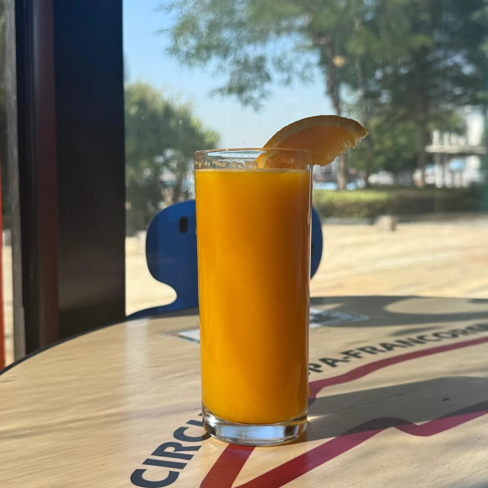 An orange-coloured drink by the café window, with the waterfront promenade outside